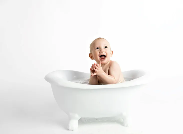 A baby boy sitting in a white clawfoot tub.