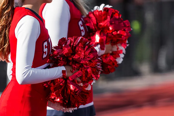 Close up photo of two cheerleaders dressed in red holding red and white pom-poms.