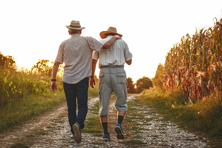 Two elders walking arm-in-arm through a corn field.