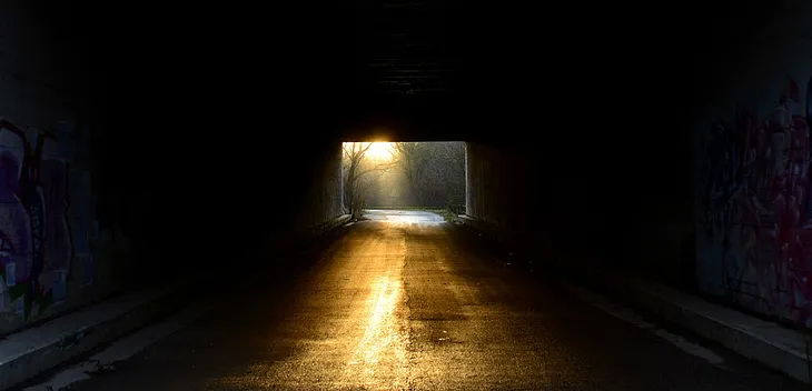 The viewer seems to be inside a dark tunnel. Light shines in the other end of the tunnel, creating a golden path forward.