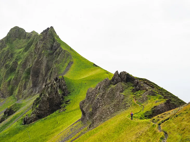 Craig stands on a grassy ridgeline that rises ahead of him.