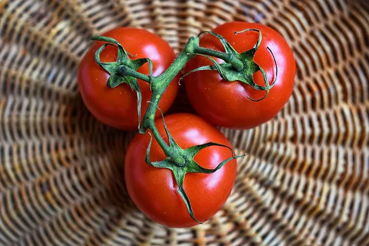 Three red tomatoes attached by a vine, sitting in a wicker basket.