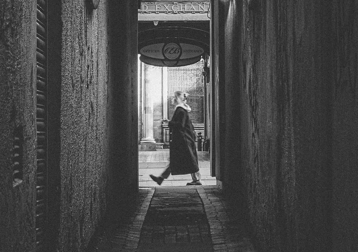 A woman passing by a black and white alleyway