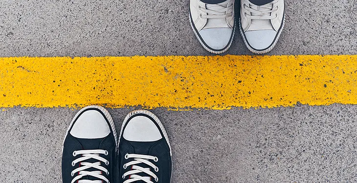 Two pairs of shoes standing on opposite sides of a yellow street line