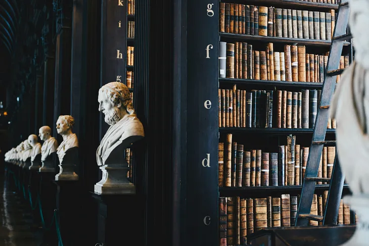 An old university library with shelves full of antique hardbound books and busts of prominent figures