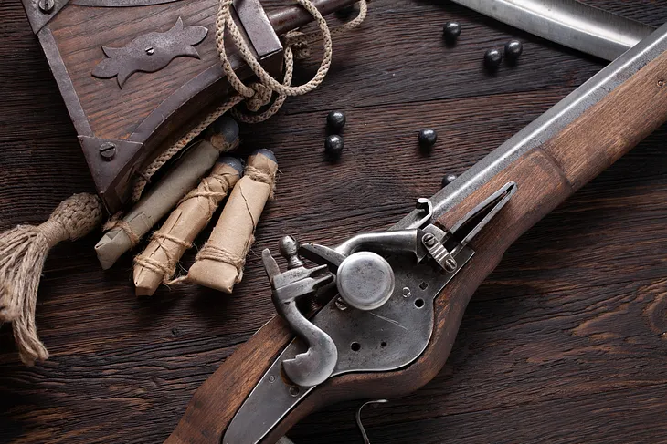 17th century ancient flintlock musket with powder flask and led bullets on wooden deck.