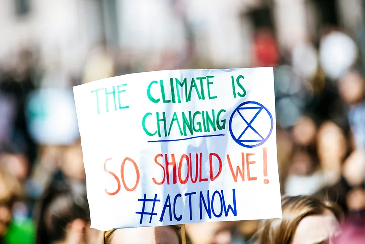 Protester holding a sign that reads ‘The climate is changing, so should we! #ActNow’ during a climate change rally.