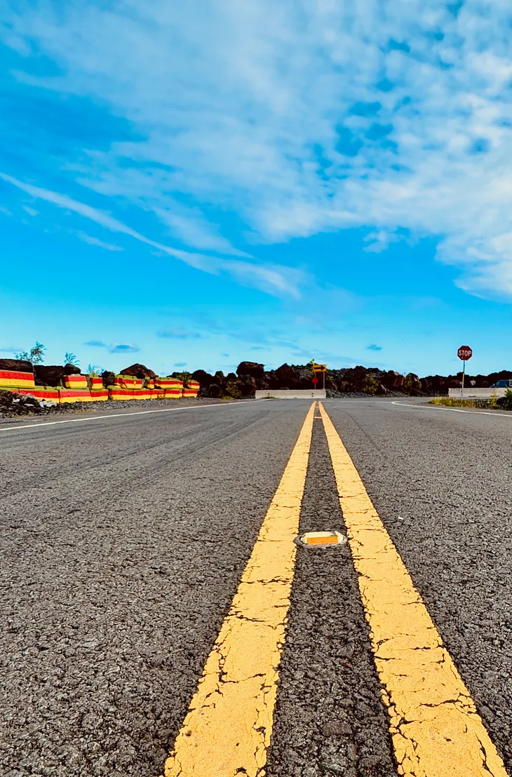 A low-angle view of a straight asphalt road with bright yellow lane lines under a blue sky, symbolizing direction and movement.