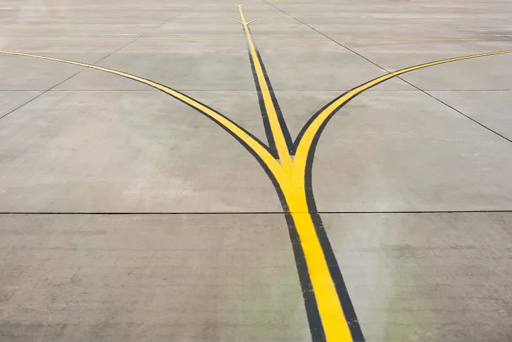 An airfield with a yellow line with black edges running through it. The line forks off and curves to the left and right, as well as continuing straight on, showing three prongs.