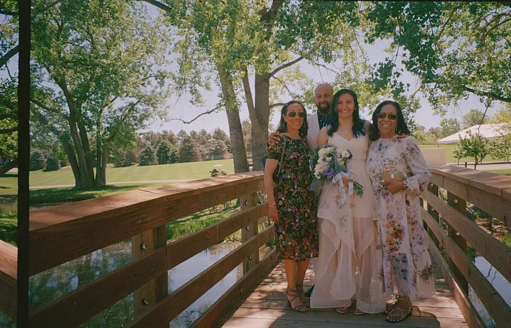 My husband, aunt, and Grandmother and I pose for a picture at our wedding. Black family standing on a bridge in a park.