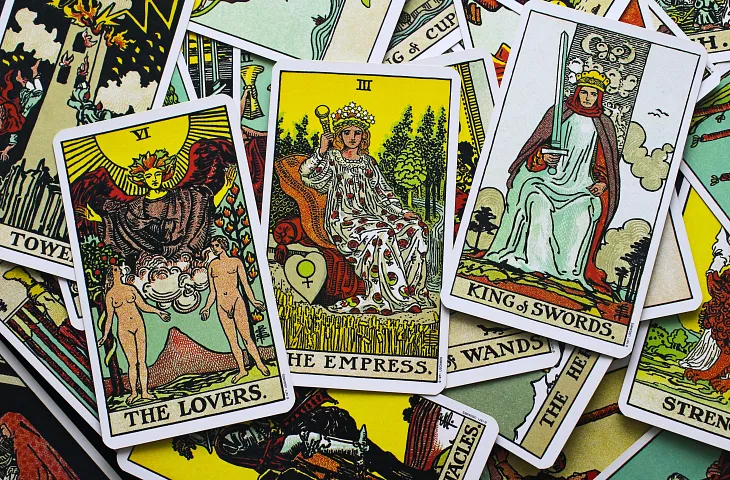 Photo by Manik Roy on Unsplash of the Empress Card between the Lovers and Kind of Swords cards on top of a messy spread of the Rider Waite tarot deck