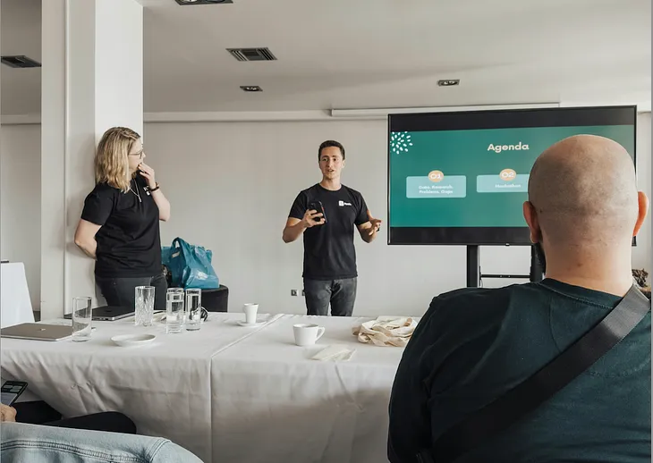 A presenter speaking in front of a projection displaying a graph in a conference room with two colleagues fully engaged.