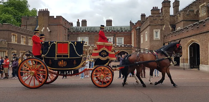 Black carriage pulled by brown horses with coachmen dressed in red