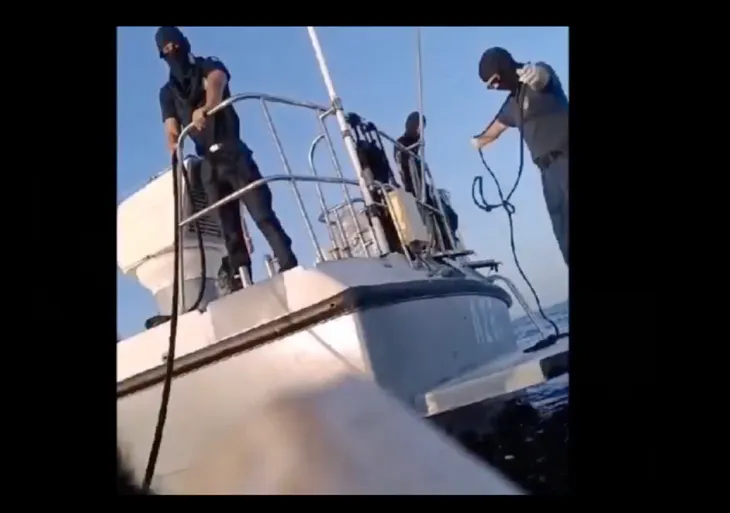 Masked men on a Greek Coastguard vessel hold ropes to keep close to a migrant boat, before removing its fuel and setting it adrift back to Turkey.