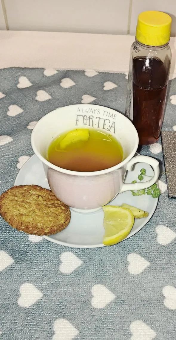 A cup of herbal tea with a slice of lemon and a biscuit on the saucer. The cup has the words ‘Always Time For Tea’ inscribed at the top.