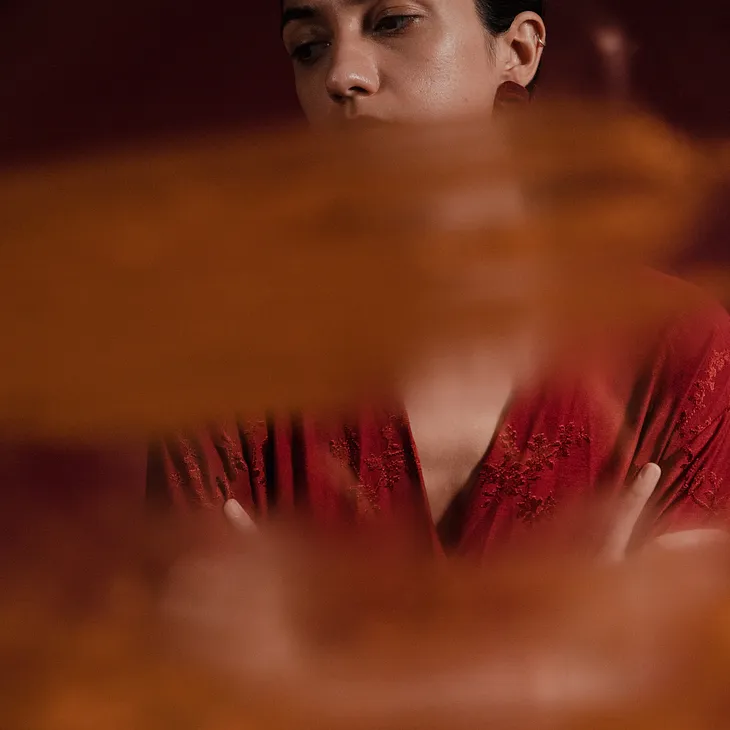 Portrait of a person in a red dress. Blurred burnt orange lines overlay the picture. Credit: Canva