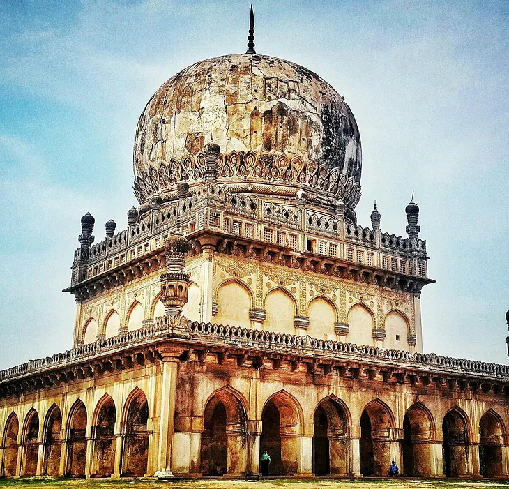 Qutb Shahi Tomb, an intricately designed monument with large domes, pointed arches, and ornate detailing, located in Hyderabad, India. This historic tomb features traditional Islamic architecture, with lush green gardens surrounding the structure, reflecting the grandeur of the Qutb Shahi dynasty.