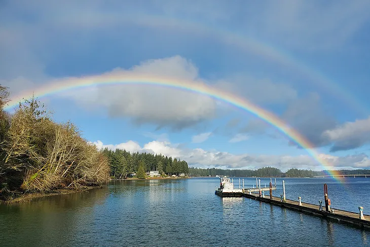 A double rainbow arches across a ship at a dock