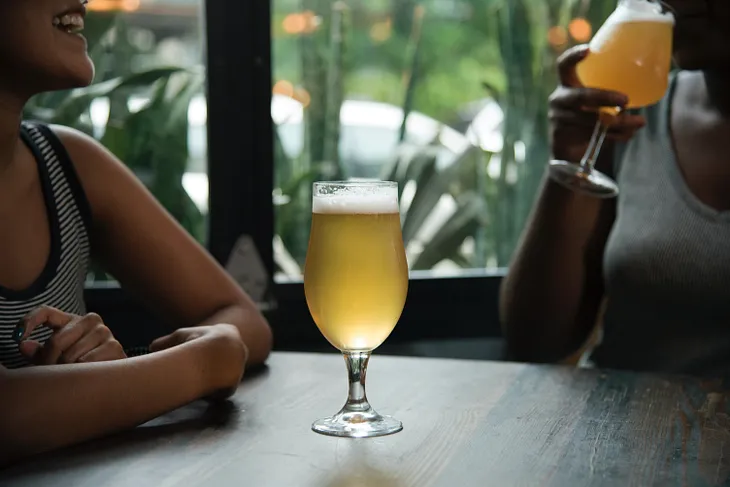 Two people sit at a table, enjoying glasses of beer