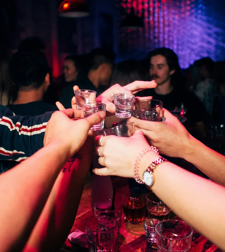 A group of people’s hands holding up shot glasses