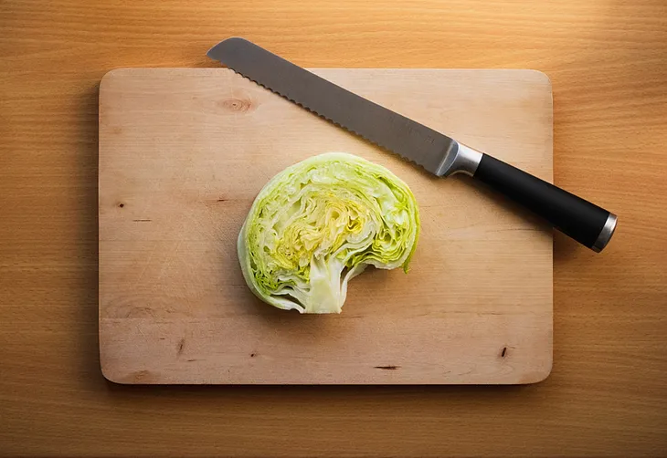 A brain shaped lice of lettuce on a cutting board next to a knife