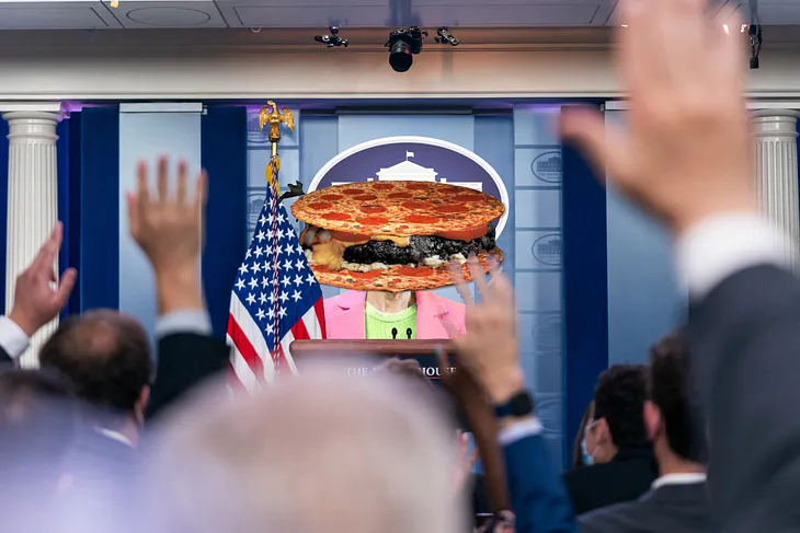 A press conference in the White House briefing room. The press secretary has been replaced with a woman’s torso topped with a ‘pizzaburger’ (a hamburger patty between two pepperoni pizzas) in place of a head.