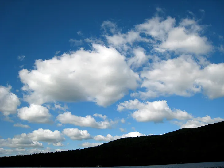 A blue sky with fluffy white clouds over a darkened shadow of a hill