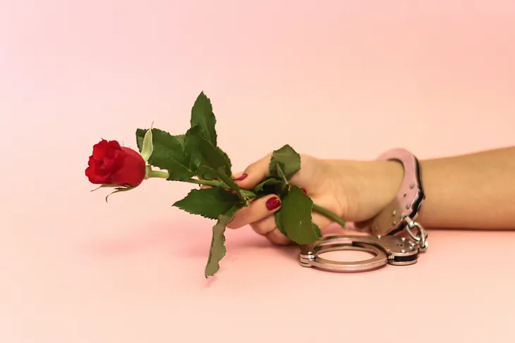 Hand holding a single rose, with a handcuff around the wrist.