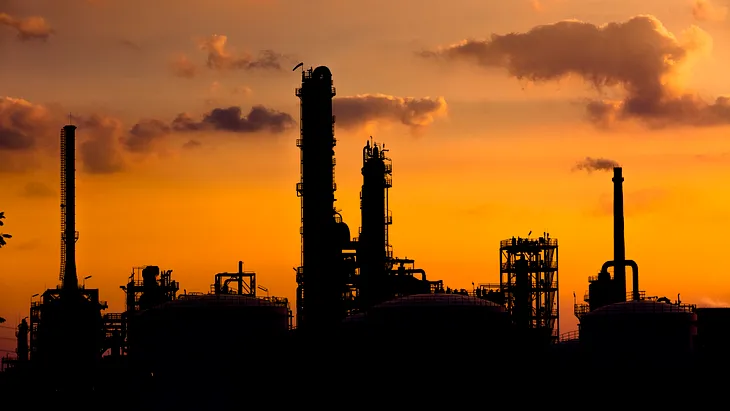 A petrochemical facility stands in silhouette against an orange sky