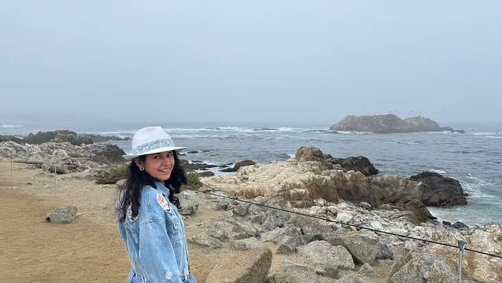 author in the picture smiling standing near seashore.