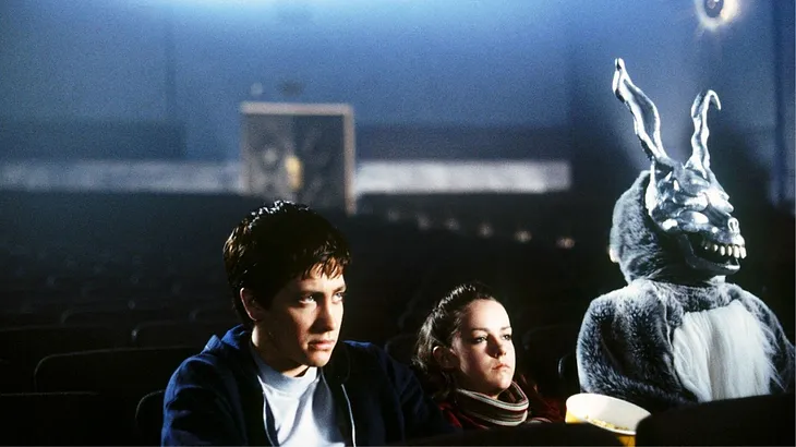 Donnie Darko, Gretchen, and Frank sit in an empty movie theater watching a film.