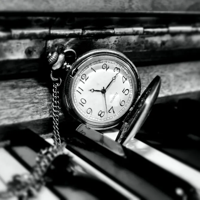 black and white photo of an antique pocket watch on piano keyboard