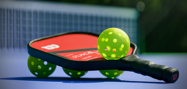 A pickleball racket sitting on three balls, with a fourth ball balanced on top