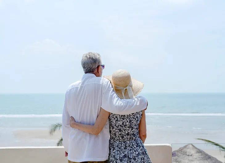 Mature couple standing together with arms around each other enjoying the ocean view.