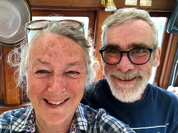 Two faces appear in the photo. Both are seniors with grey hair and both are smiling.