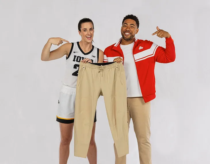 Picture of Caitlin Clark and Jake from State Farm smiling together and holding up a pair of sweat-pants.