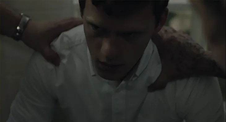 A close-up of Jared (portrayed by Lucas Hedges) as he stares while two characters from the conversion camp put their hands on his shoulders and pray.