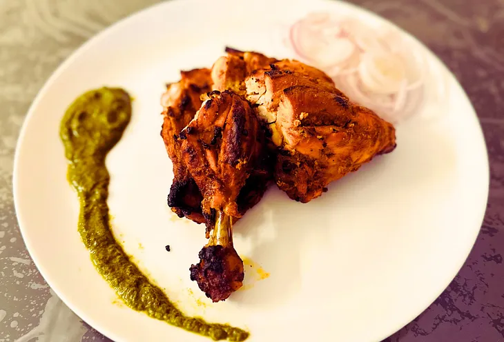 A plate of Tandoori Chicken with coriander chutney and onions.