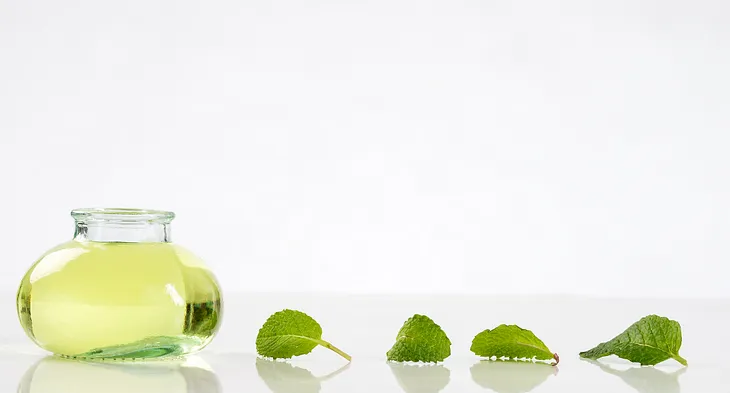 Container of peppermint oil with peppermint leaves trailing behind it.