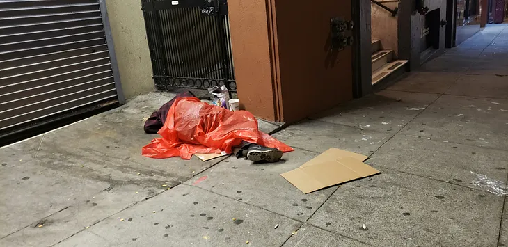 man sleeping on sidewalk under plastic bag