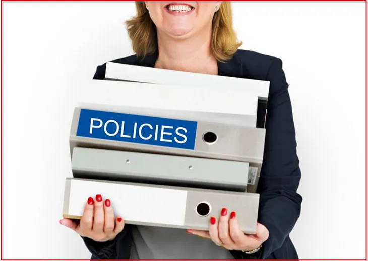 A photo of a business woman carrying a stack of binders, one of which is labeled as “policies.”