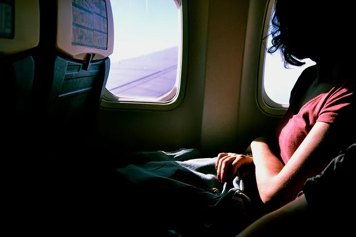 a woman in a read shirt sitting in a train and looking out of the window with the sun shining on her