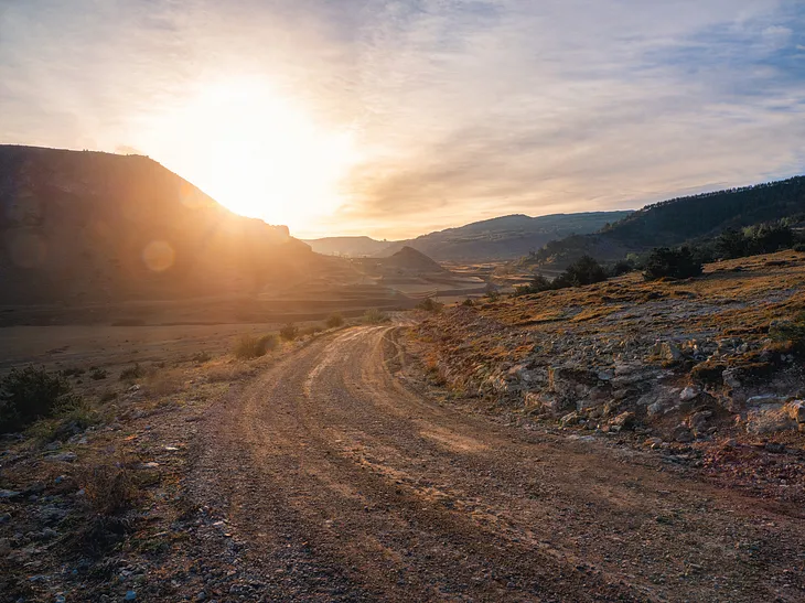 A desert road at sunset, mountains in the background.