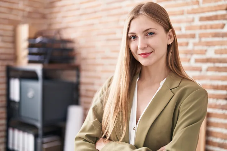 Young woman with long hair looks capable, slight smile, brick background