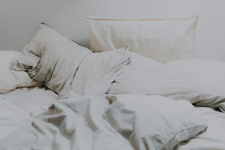 Landscape shot of a messy, slept-in bed, with scattered white pillows