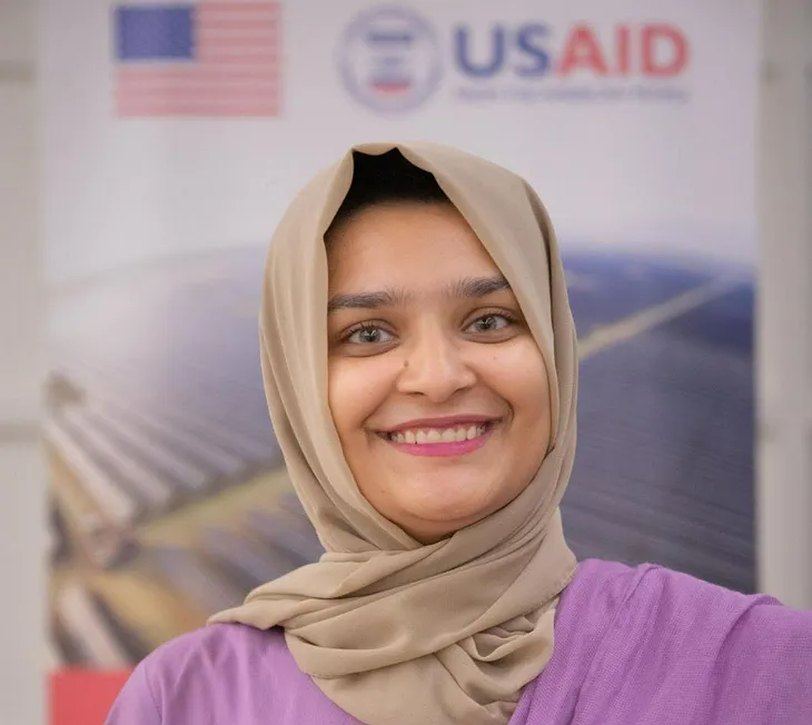 Closeup of a woman’s face in front of the USAID logo and American flag