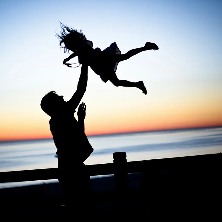 A father playfully tossing his young daughter at sunset.