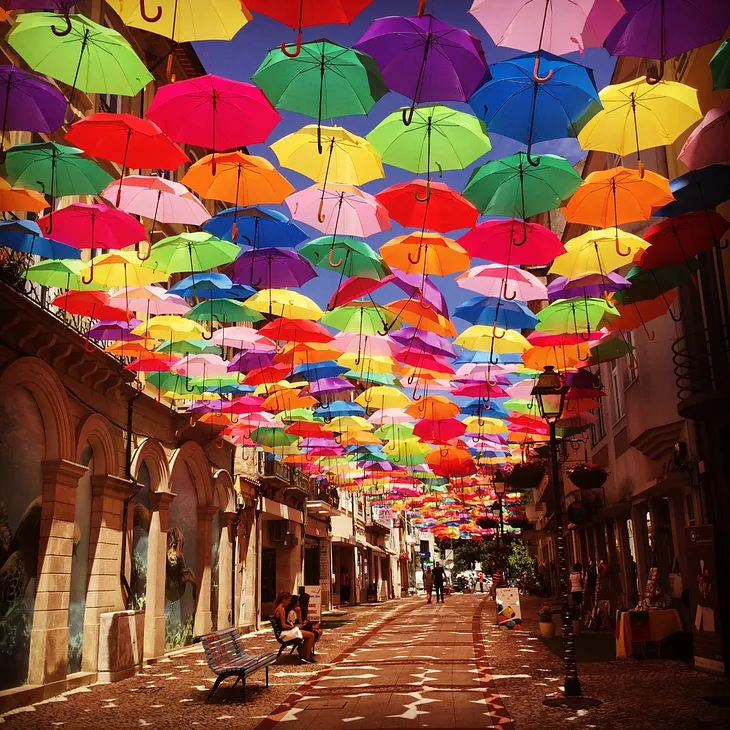 the main walking street in Agueda, Portugal with hundreds of umbrellas strung up high like a canopy of colour