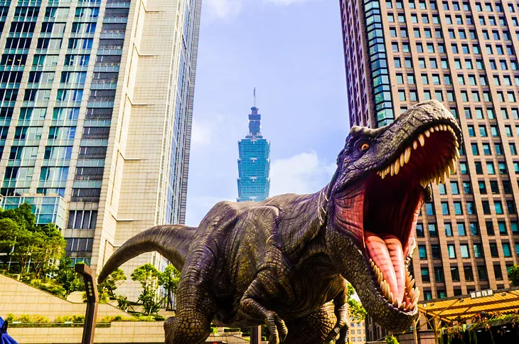 A Tyrannosaurus Rex is in a city, roaring it up