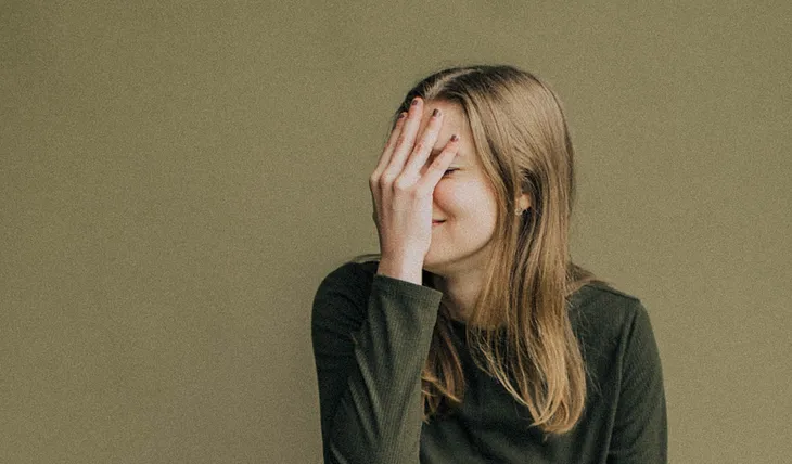 An embarrassed woman covering her face with one hand